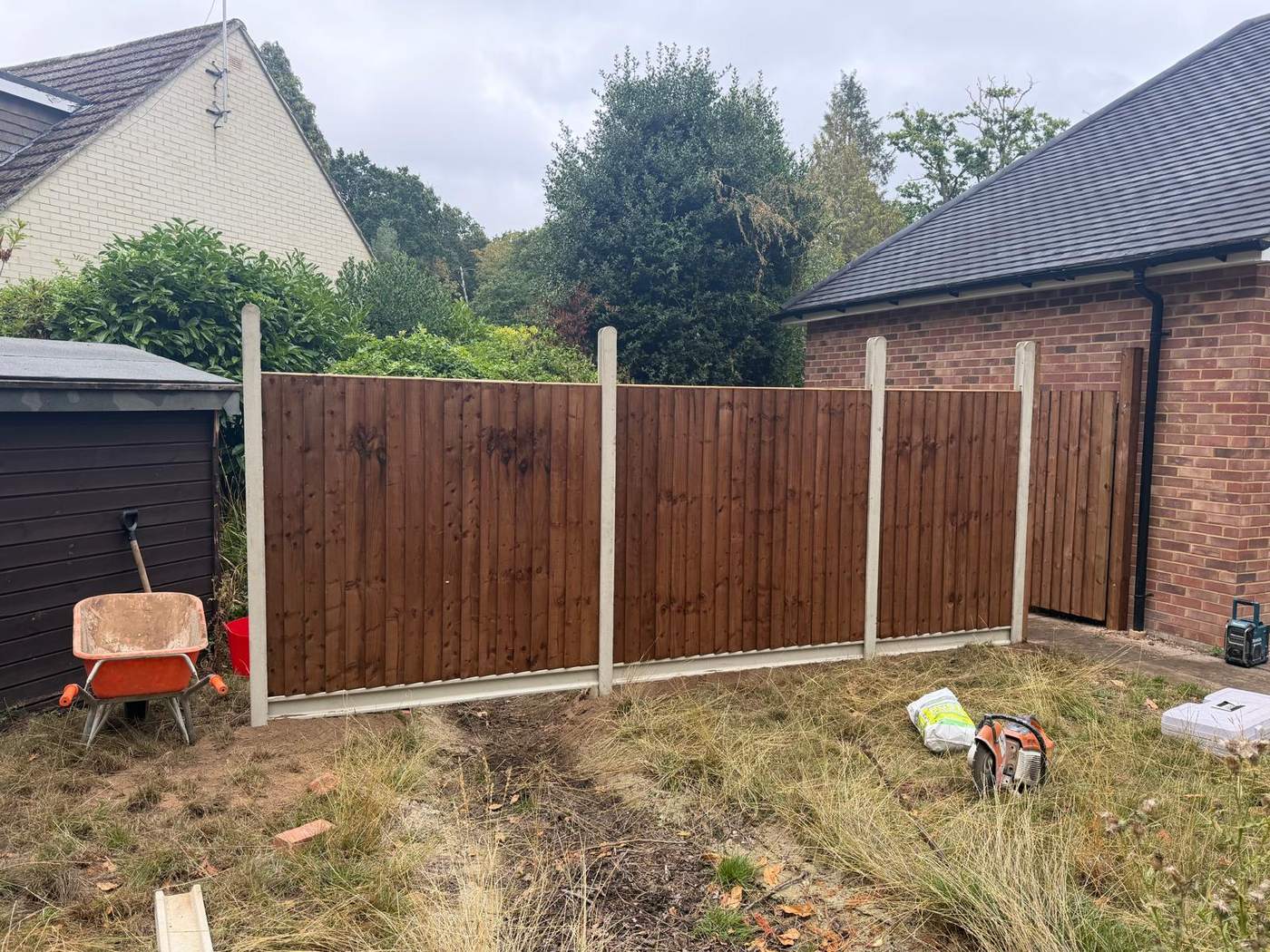 New stained closeboard fence panels in concrete posts running between a garage and a shed