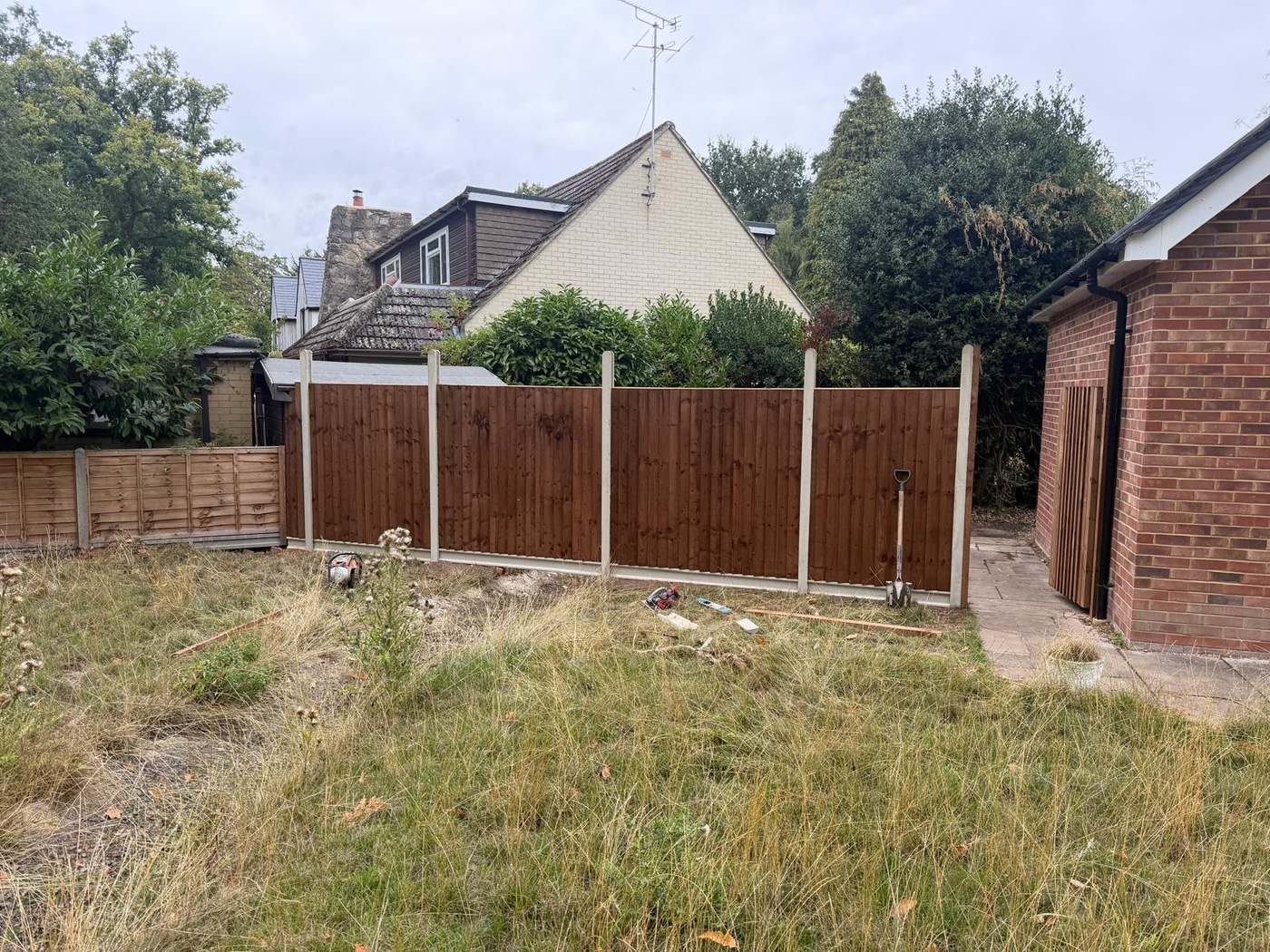 Run of stained closeboard fence panels on concrete posts across the width of a back garden