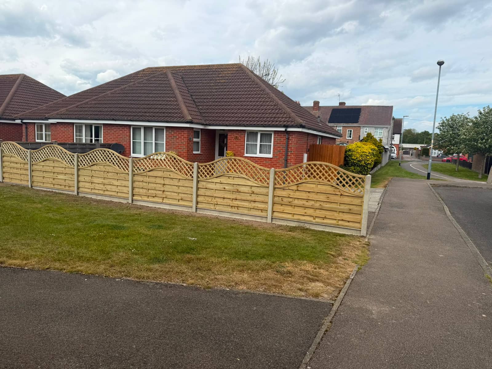 Wave top lattice fence panels in concrete posts across the front of a bungalow
