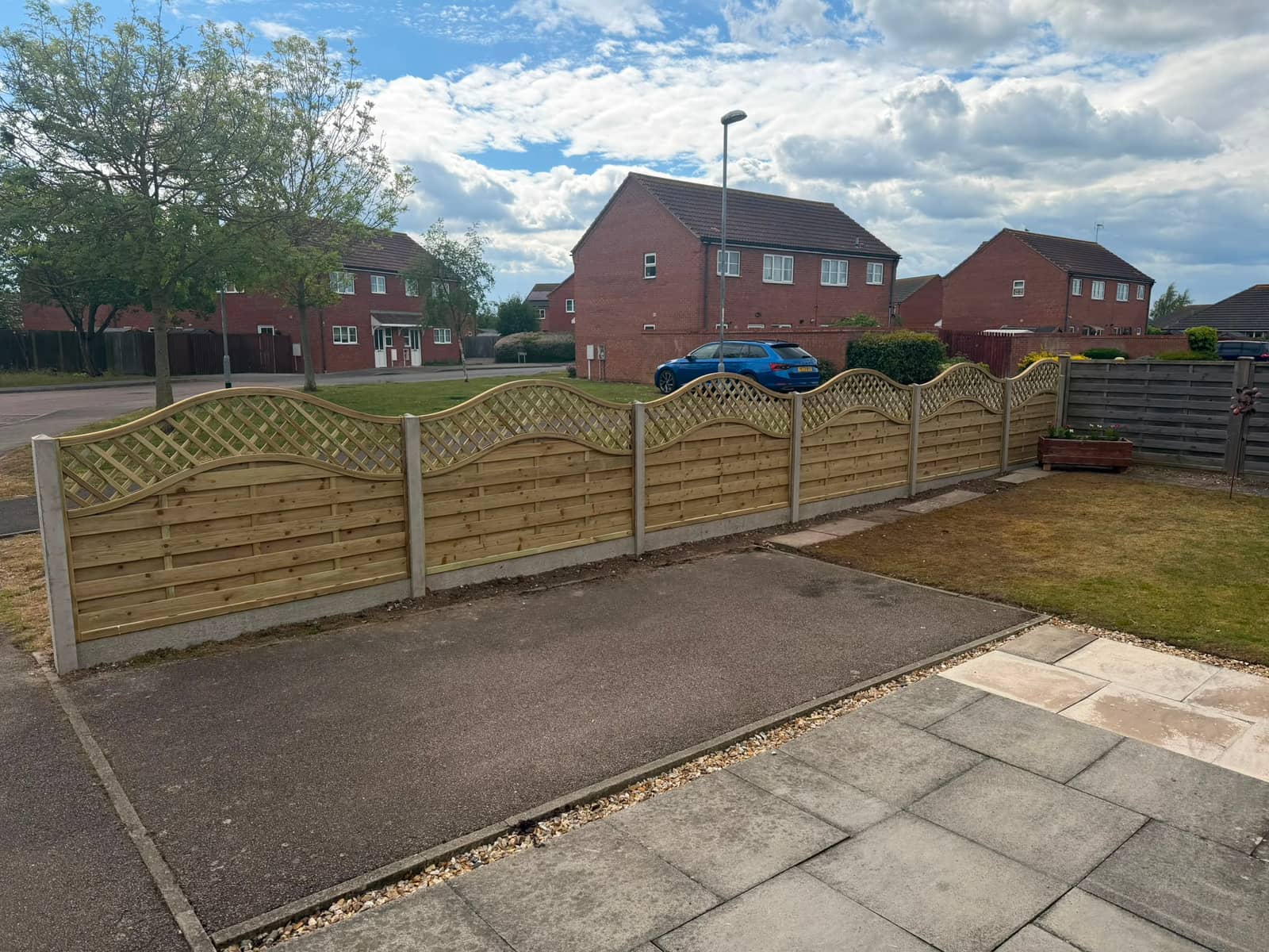 Long run of wave top fence panels on concrete posts beside a newly paved drive