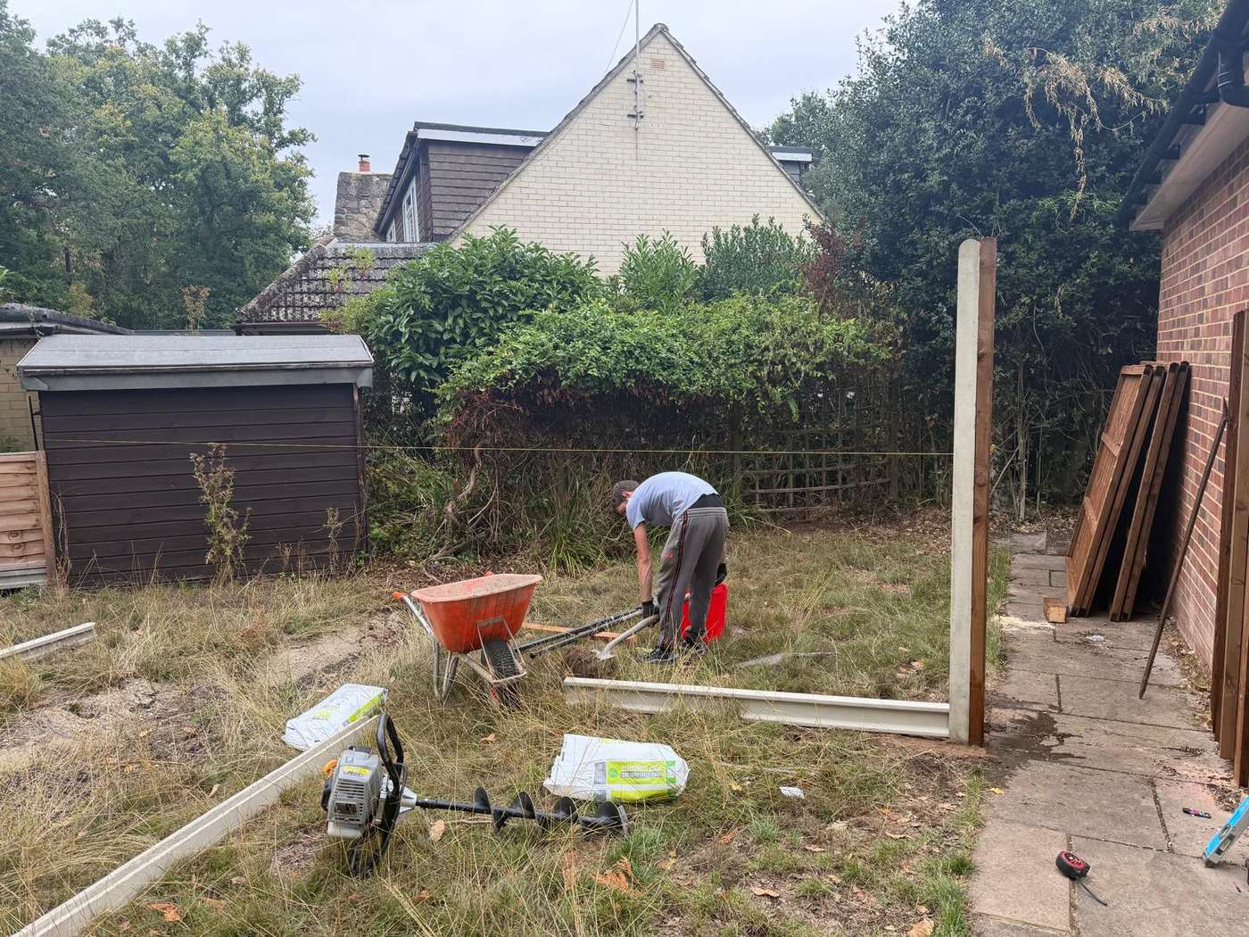 Overgrown back garden being cleared, first post set and new panels stacked ready