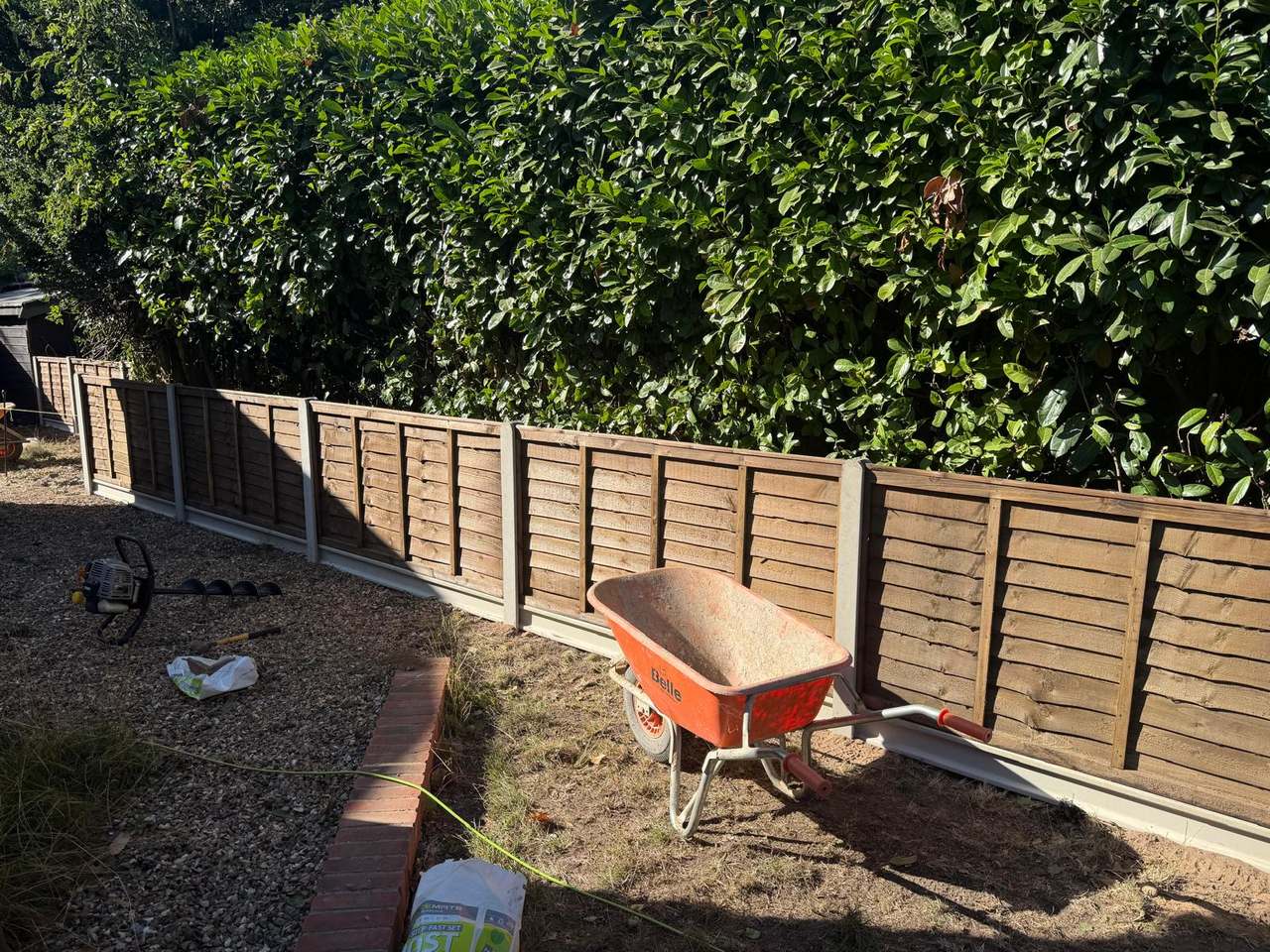 Run of lap fence panels in concrete posts set below a mature laurel hedge
