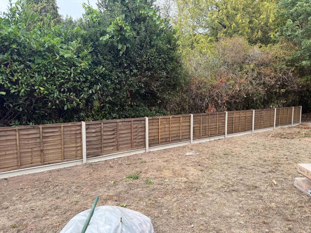 New lap fence panels and concrete posts running along a cleared garden boundary