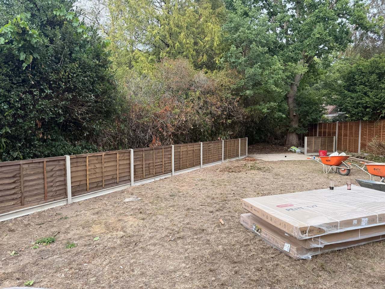 Two boundaries of a cleared back garden fenced in lap panels on concrete posts