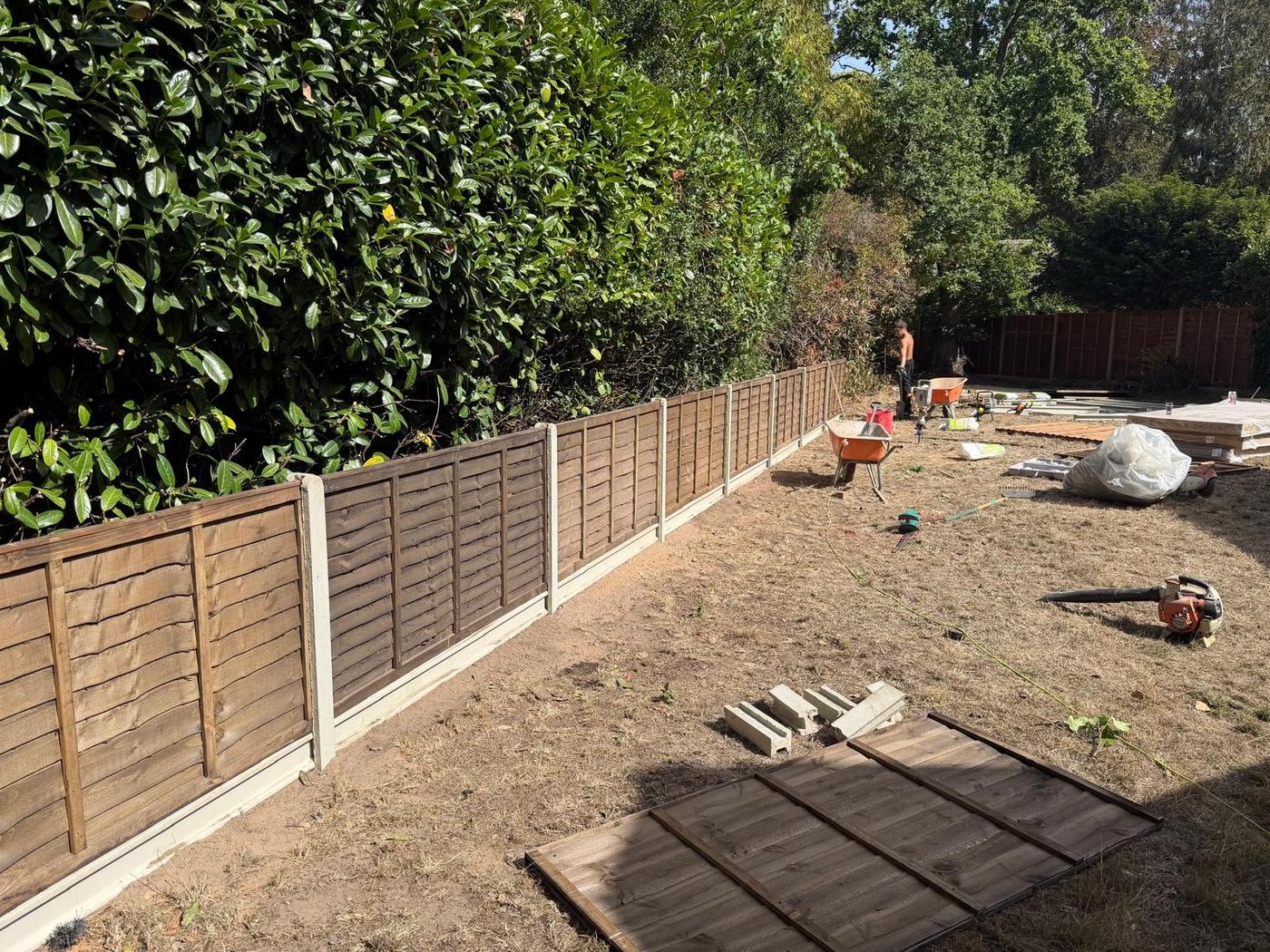 Lap fence panels on concrete posts running below a laurel hedge