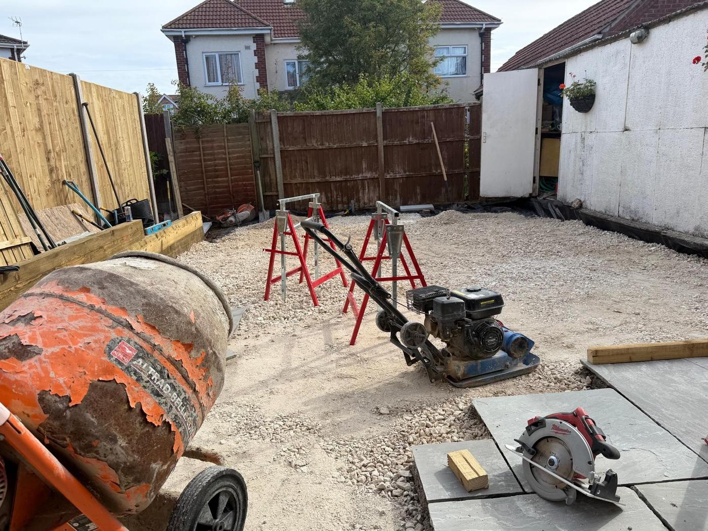 Levelled sub-base with a cement mixer, compactor plate and paving slabs ready to lay