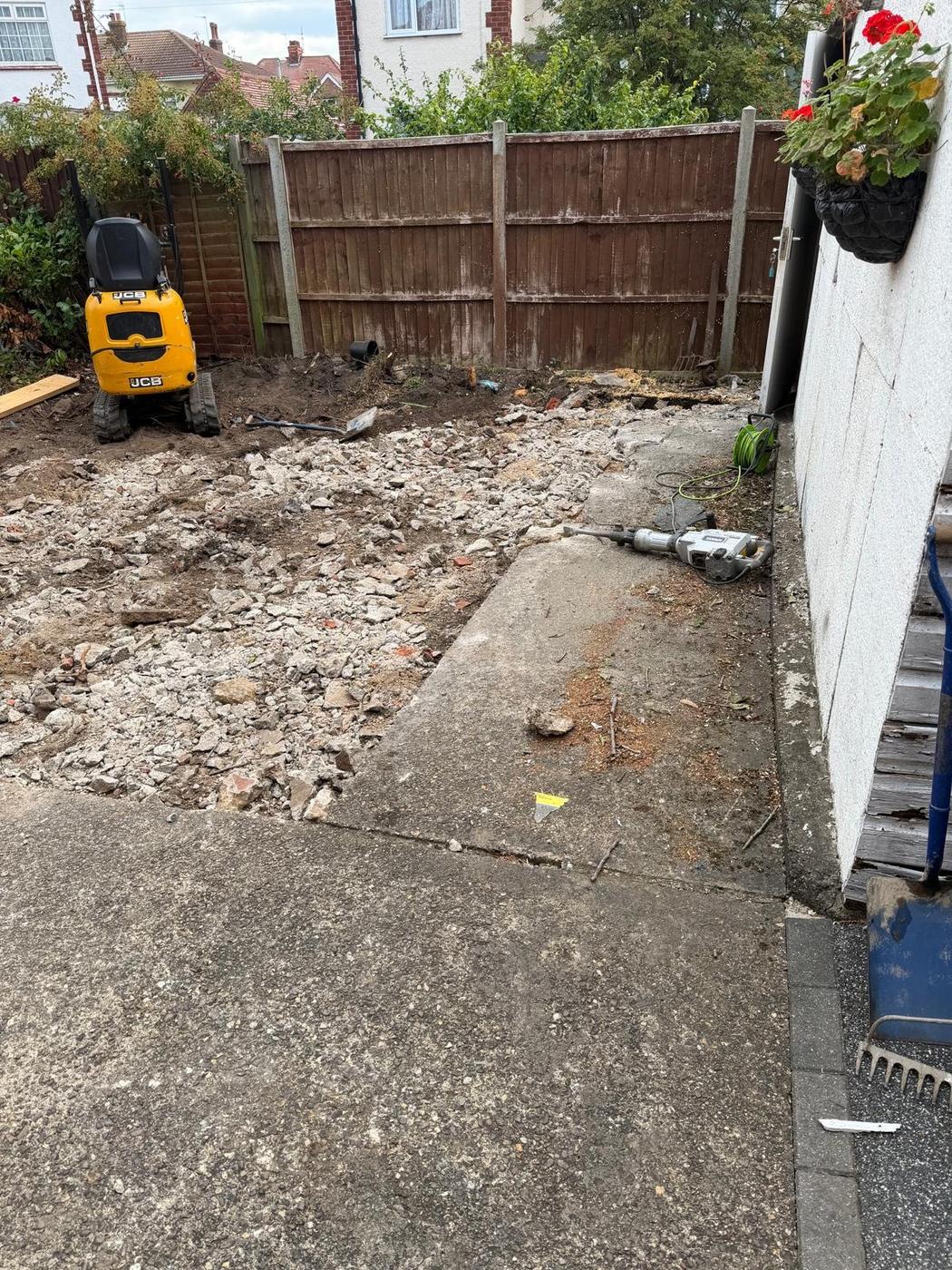 Old concrete yard being broken out with a mini digger parked by the fence