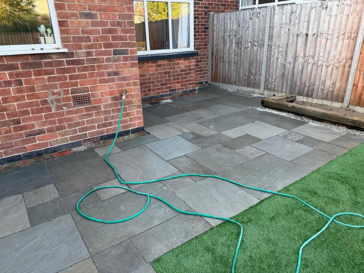 Grey paving and artificial lawn meeting at the corner of a brick house