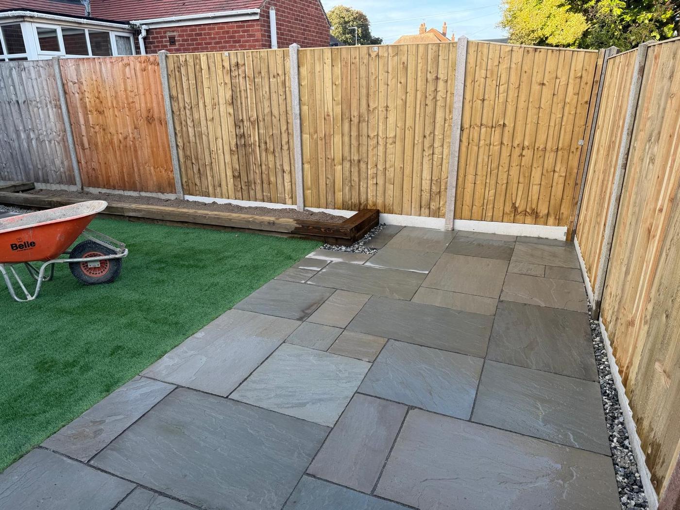Garden corner with grey paving, artificial lawn, timber sleeper edging and closeboard fence