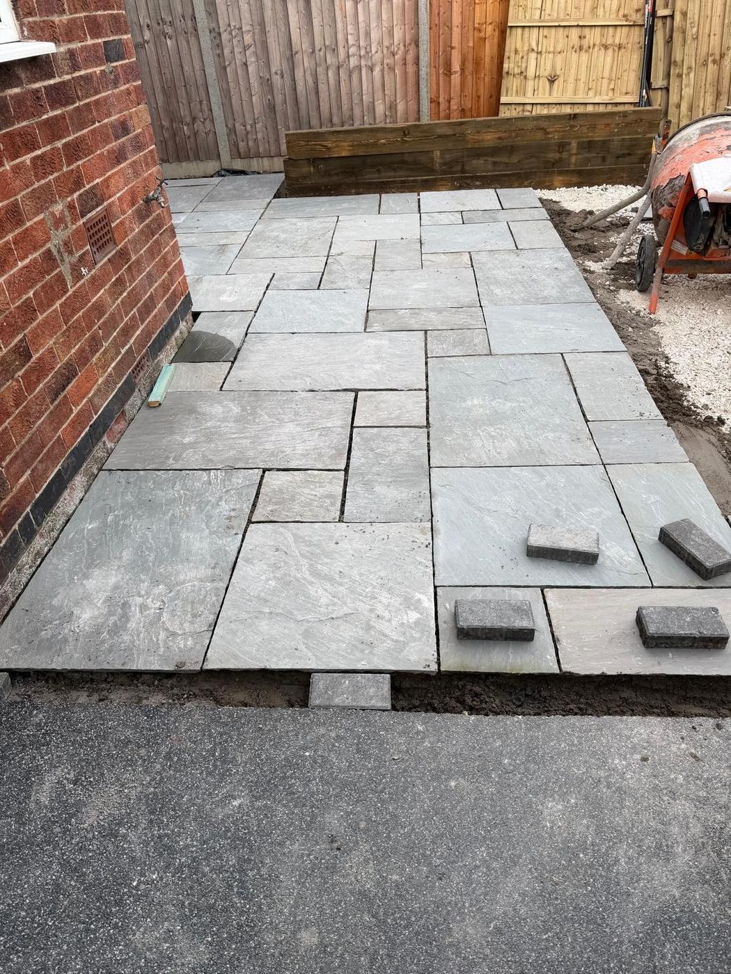 Grey paving laid in a random pattern along the house wall up to a timber sleeper edge