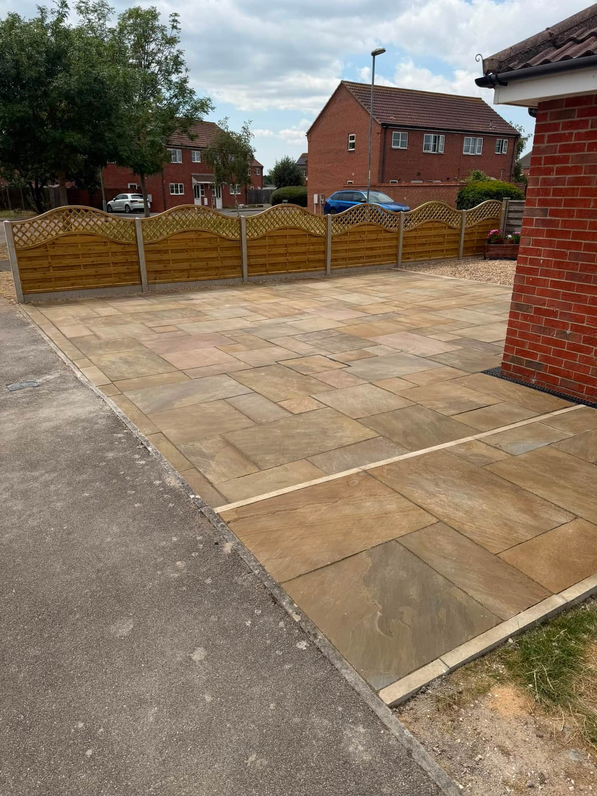 Sandstone driveway with a run of new wave top fence panels along the boundary