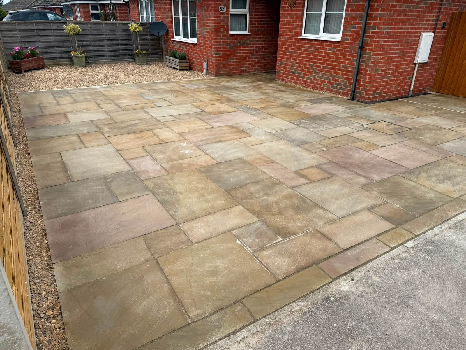 Riven sandstone patio laid across a front garden, gravel border along the house wall