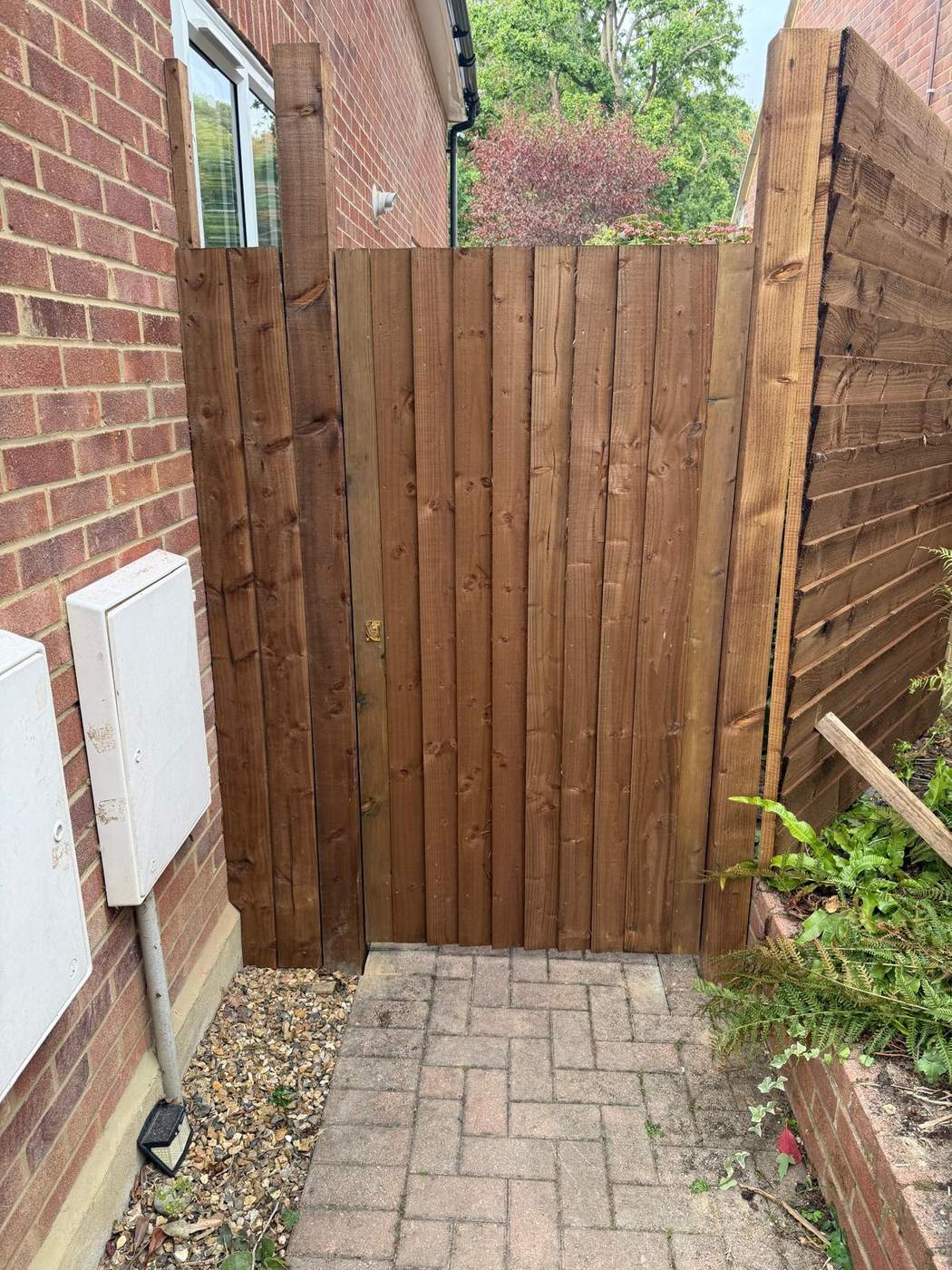 Closeboard side gate hung against the brick house wall above a block paved path